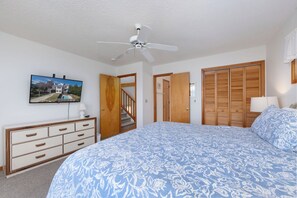Un dormitorio con una cama, un aparador, un ventilador de techo, un televisor y armarios de madera.