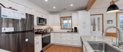 A modern kitchen with white cabinets, stainless steel appliances, a granite countertop, and a wooden floor.
