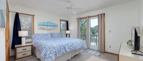 A bedroom with a bed, a ceiling fan, a desk with a computer, and a window with curtains.