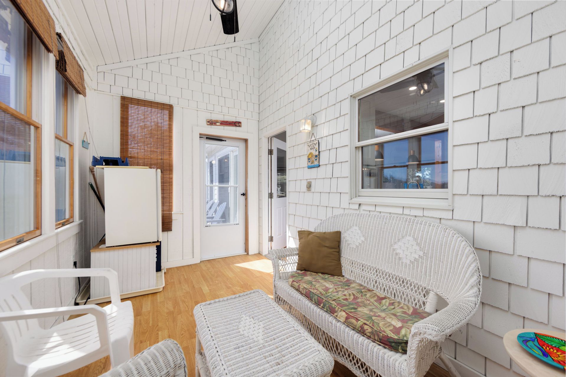 A room with white brick walls, a white wicker sofa with a floral cushion, a white plastic chair, and a small table with a colorful plate.
