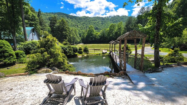 Un entorno exterior tranquilo con un mirador de madera, dos sillas Adirondack y un estanque.