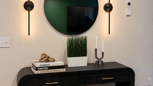 Una moderna consolle con uno specchio grande, due luci a parete, una piccola pianta in vaso, un portacandele e un oggetto decorativo.
