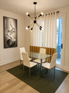 A modern dining area with a glass table, white chairs, a black chandelier, and a large abstract painting on the wall. - Urban Stylish 4 Story Townhome in Downtown Atlanta with Rooftop + 2 car garage (Atlanta)