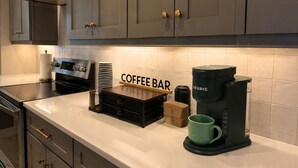 Una cucina con angolo caffè, che include una macchina da caffè Keurig, una tazza verde e una pila di piatti.
