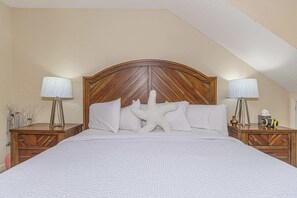 Une chambre Ă coucher avec une tĂȘte de lit en bois, une literie blanche, deux tables de chevet avec des lampes et un coussin en forme dâĂ©toile de mer.