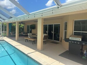 A covered outdoor area with a pool, a barbecue grill, and seating arrangements.