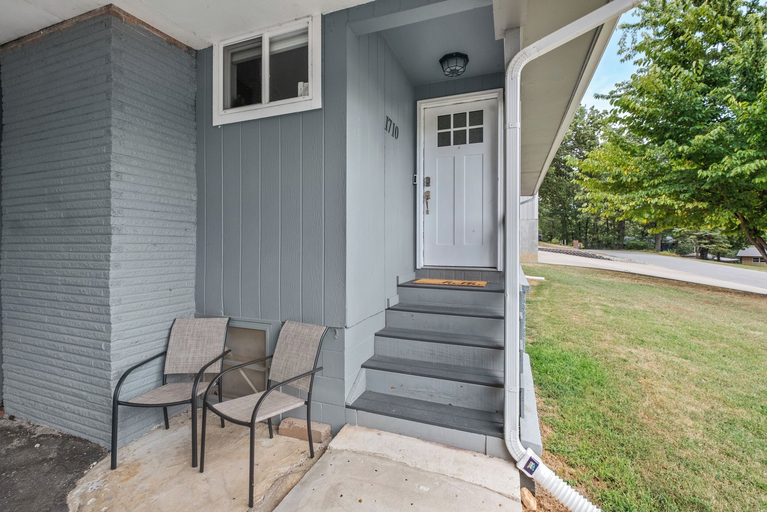 A gray house with a front porch, a white door, and a set of stairs leading to the entrance.