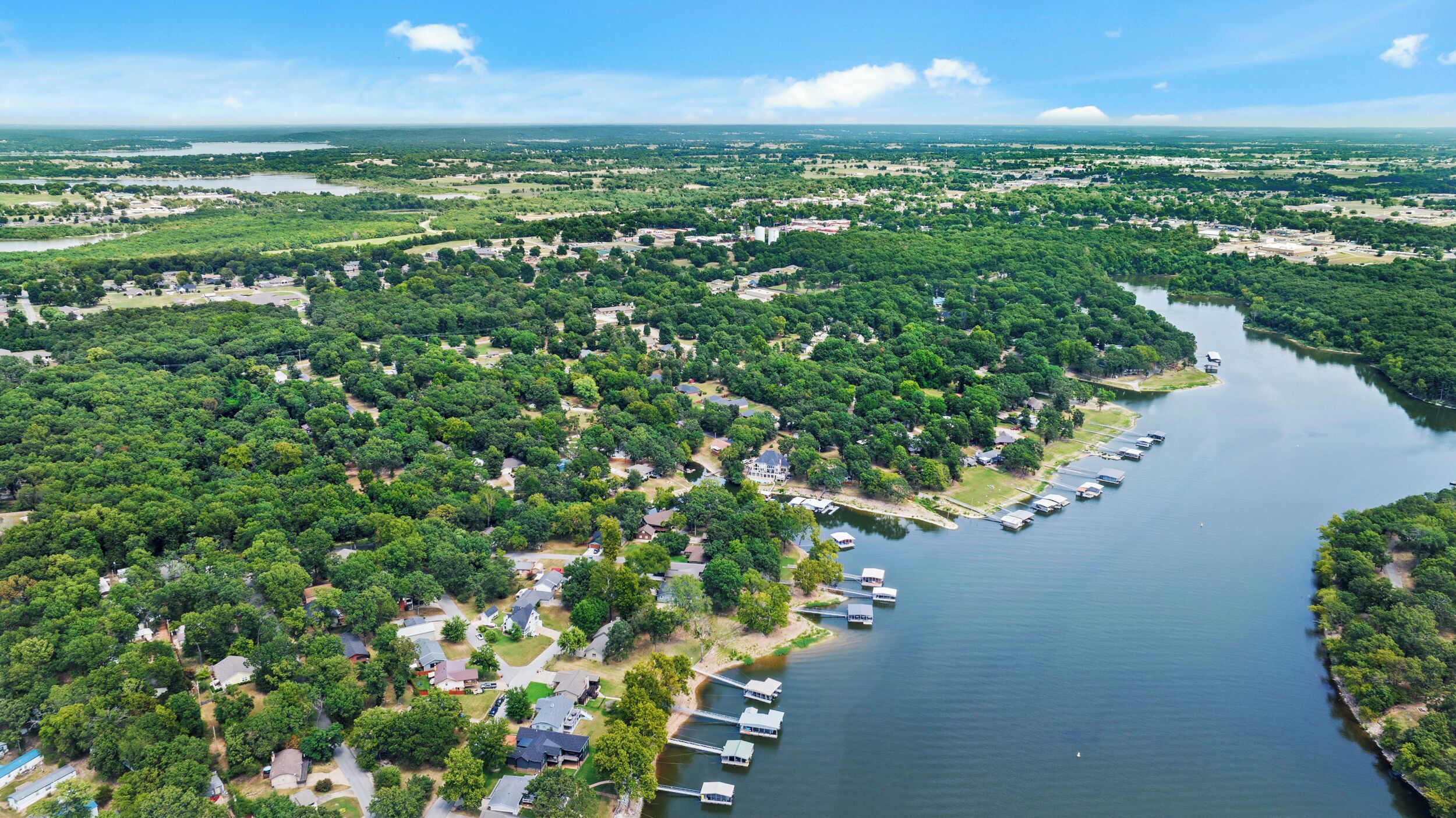 Luchtbeeld van een woongebied met een rivier, bootjes afgemeerd langs de oever, en een mix van huizen en open velden.