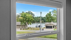 Udsigt fra et vindue over et boligområde med en sø, en anløbsbro og et hus med garage.