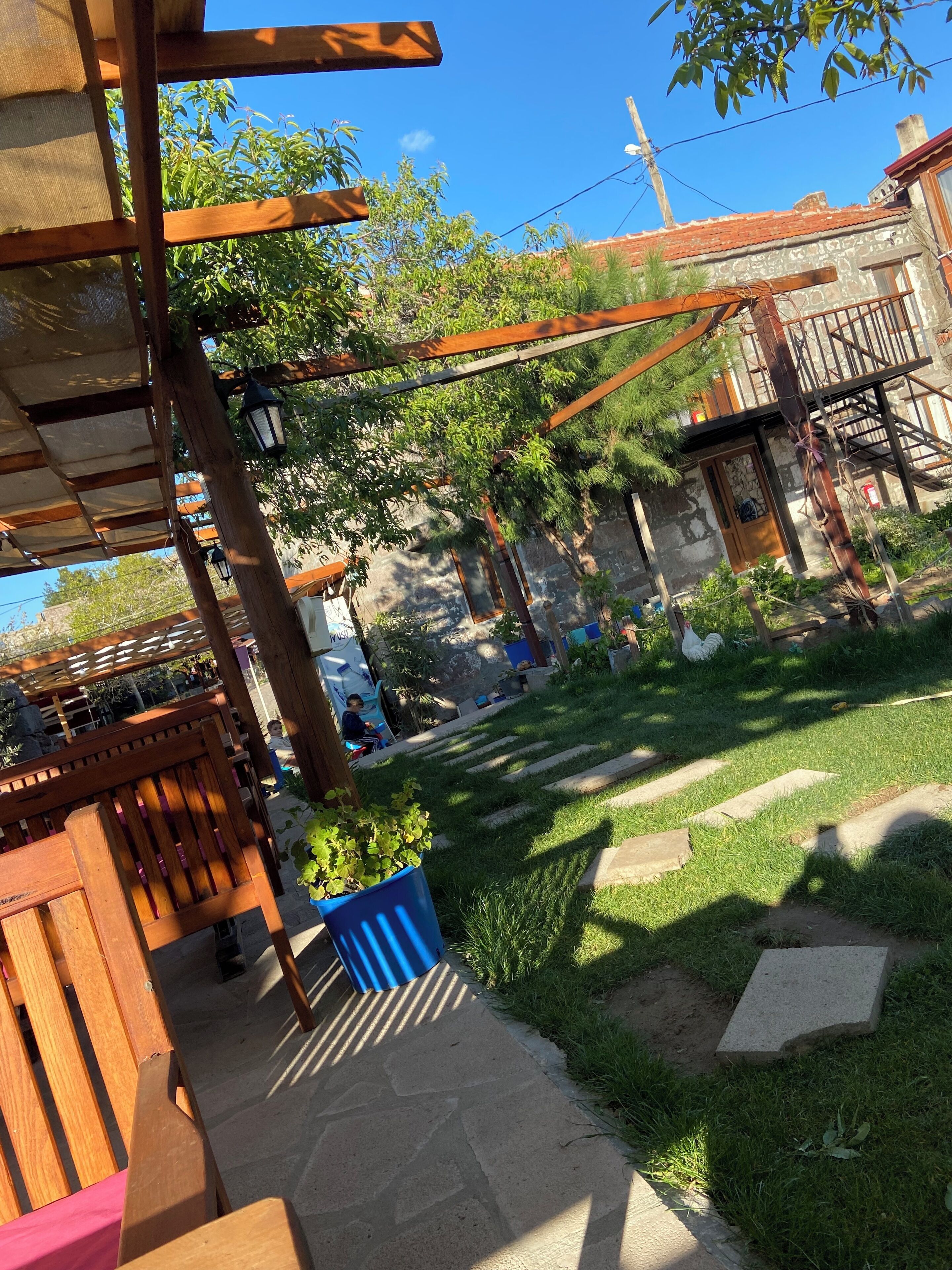 A courtyard with a wooden pergola, a blue planter, and a stone pathway.