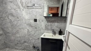 Un bagno con un WC bianco, un lavandino con uno specchio sopra, un mobile nero sotto lo specchio e uno spazio doccia con una vasca bianca.