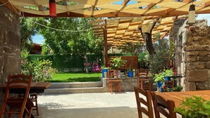 Una terrazza esterna con tavoli e sedie di legno, un muro in pietra e piante in vaso.