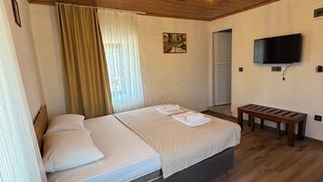 A room with a wooden ceiling, a bed with white linens, a bedside lamp, a TV mounted on the wall, and a wooden bench.