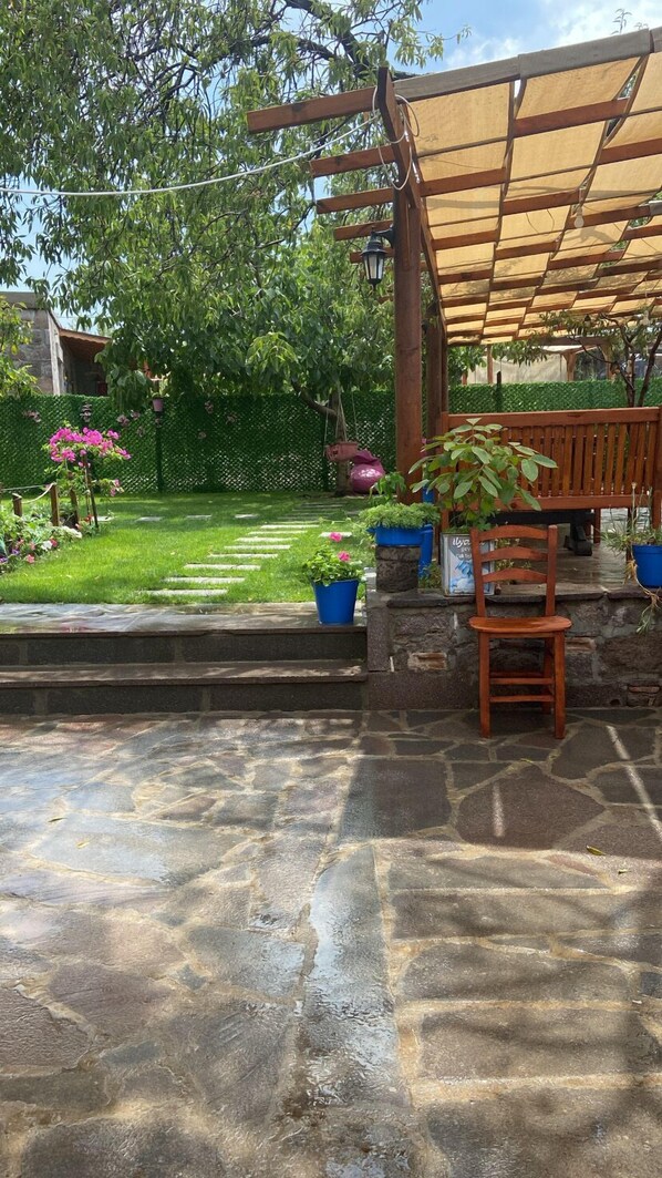 Un patio con suelo de piedra, mobiliario de madera y plantas en macetas.