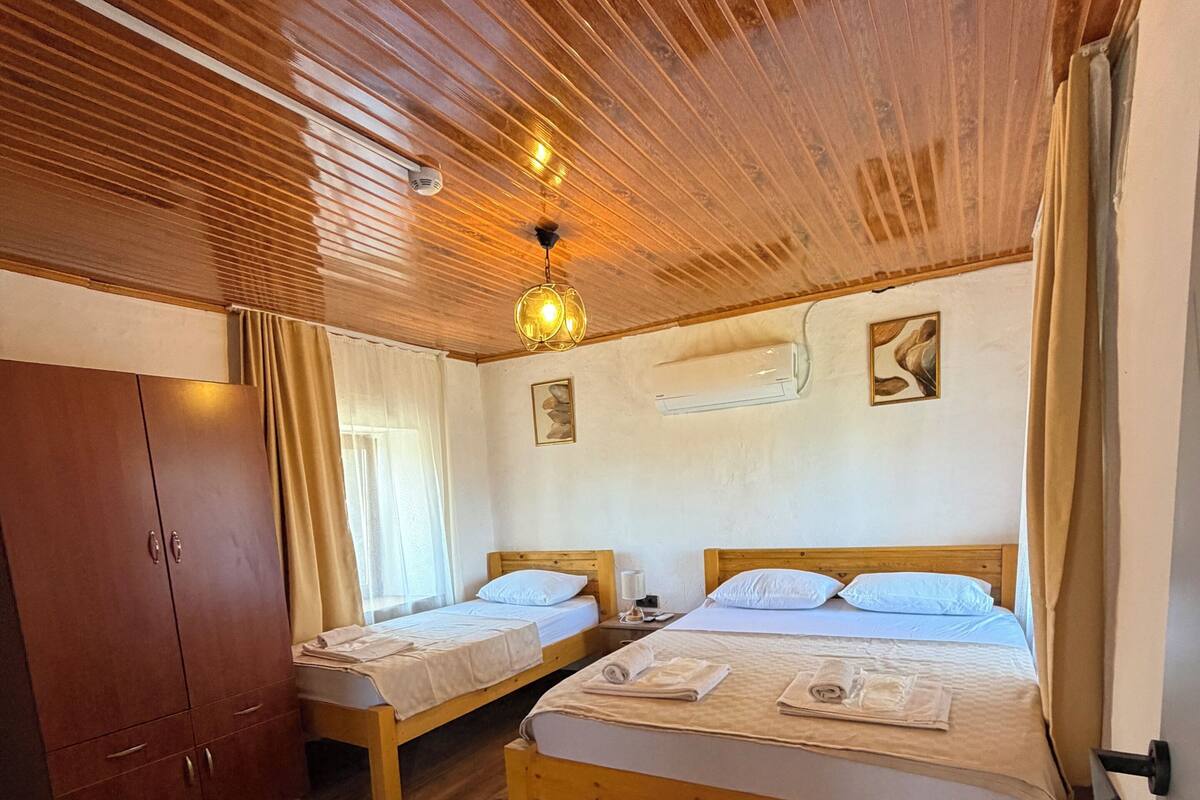 A room with two wooden beds, a wooden wardrobe, a bench, and a ceiling light fixture.