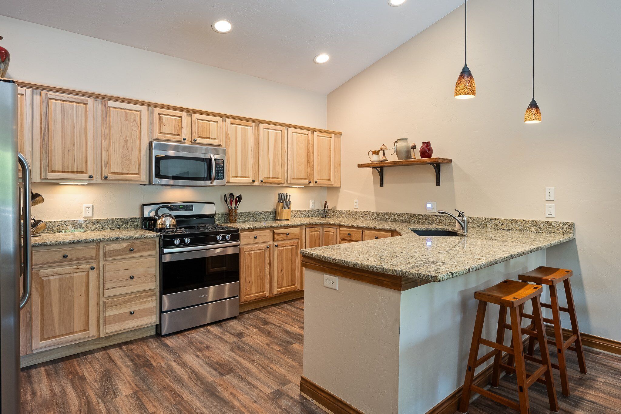 A kitchen with wooden cabinets, stainless steel appliances, granite countertops, and a bar stool.