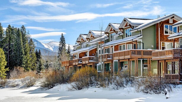 A row of wooden cabins with balconies, set against a snowy mountain backdrop.