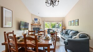 A dining area with a wooden table and chairs, a fireplace, and a sofa in the background.