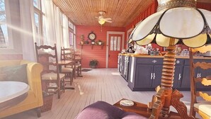 A cozy cabin interior with a wooden ceiling, a dining area with chairs and a table, and a kitchen with cabinets and a stove.