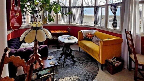 A cozy living room with a wooden ceiling, a yellow sofa, a red guitar, and a large window with checkered curtains.