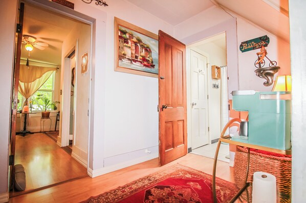 A hallway with a wooden door, a painting of a coastal scene, a sign reading "Peddy's," and a vintage-style refrigerator.