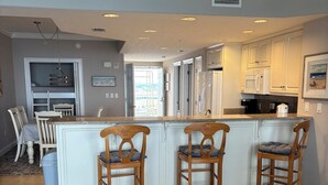 A kitchen with a central island, wooden chairs, and a dining area with a table and chairs. - Best View On The Beach.  Complimentary beach service. (Panama City Beach)