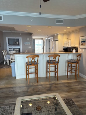 Una cocina con una isla central, sillas de madera y una zona de comedor con una mesa y sillas.