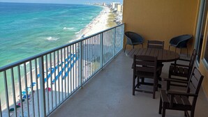 A balcony with a view of the beach and ocean. There are wooden tables and chairs, and a blue lounge chair. - Best View On The Beach.  Complimentary beach service. (Panama City Beach)