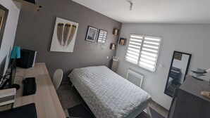 Un dormitorio con cama, un escritorio con computadora, una silla, una ventana con persianas y adornos en la pared.