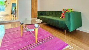 Ein modernes Wohnzimmer mit Glastisch, einem grünen Sofa und einem violetten Teppich.