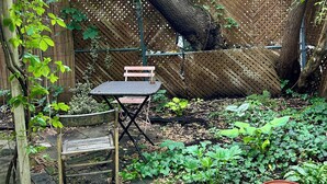 Ein Garten mit einer Holzbank, einem Tisch und einem großen Baum.