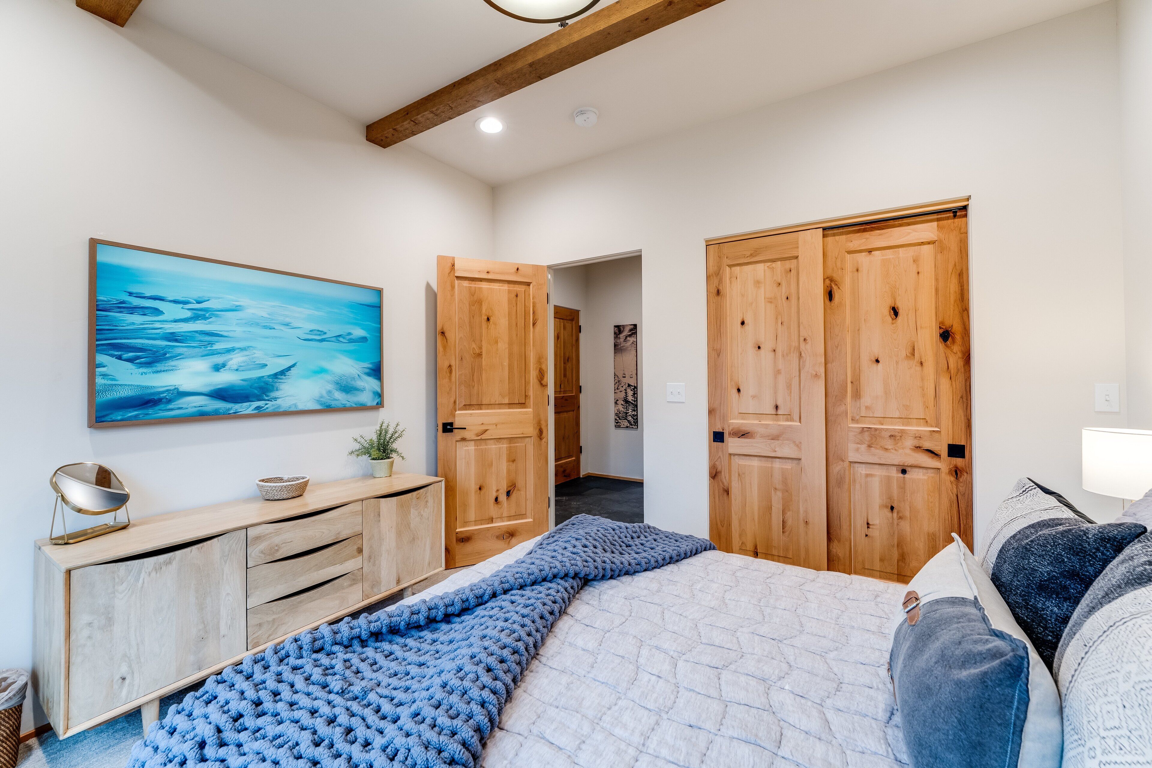 A bedroom with a bed, a wooden wardrobe, a dresser, a painting, and a hallway.