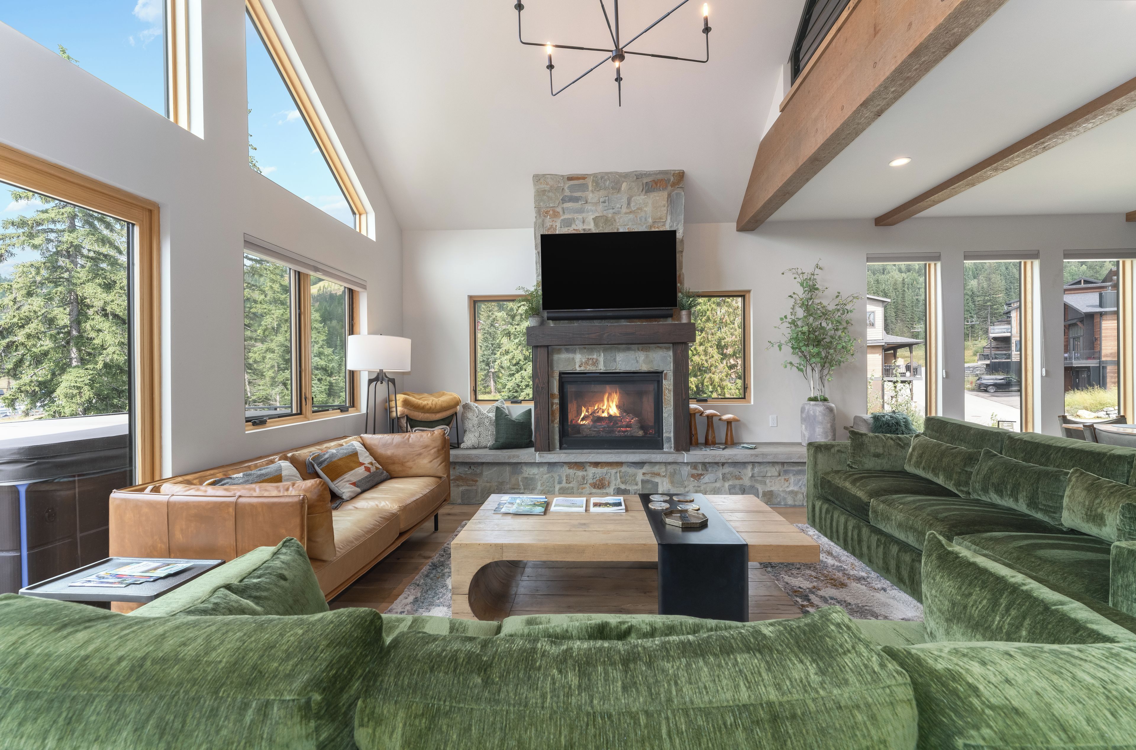 A spacious living room with a fireplace, large windows, and a modern chandelier.