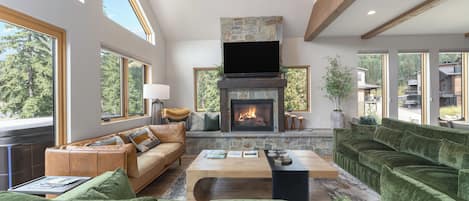 A spacious living room with a fireplace, large windows, and a modern chandelier.