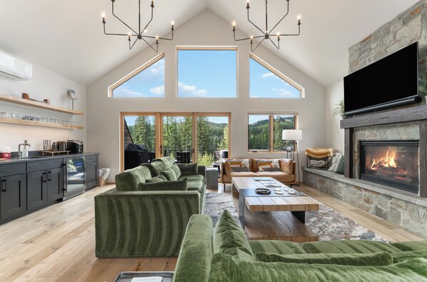 A spacious living room with a large green sectional sofa, a wooden coffee table, and a stone fireplace.