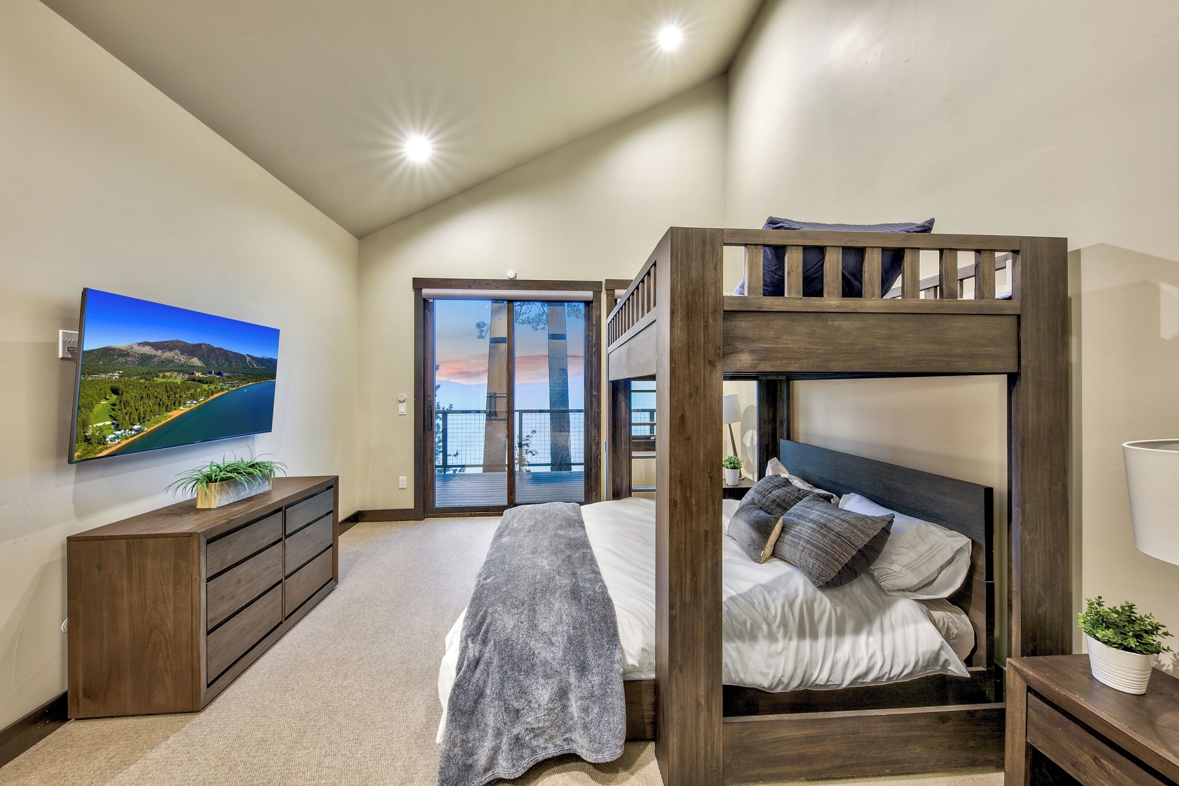 Un dormitorio con una cama litera, un televisor de pantalla plana, un aparador y vistas a un balcón.
