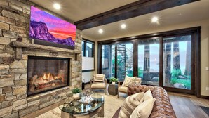 Una sala de estar con chimenea de piedra, un televisor grande montado encima y vistas a un paisaje montañoso a través de puertas corredizas de vidrio.