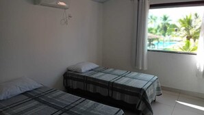 Quarto com duas camas, uma janela com cortinas e um aparelho de ar condicionado na parede.