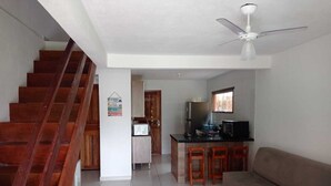 Uma sala de estar com sofá, mesa de centro de vidro e área de cozinha com fogão, micro-ondas e geladeira.