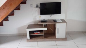 Quarto com uma escrivaninha de madeira, televisão na parede e uma escada.
