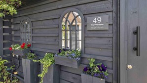 A wooden building with a number 49 sign, a window with a decorative arch, and flower boxes with various plants. - Garden Room With Parking By My Getaways (Lancing)