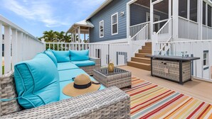 A covered outdoor seating area with a sofa, a wicker chair, and a small table.