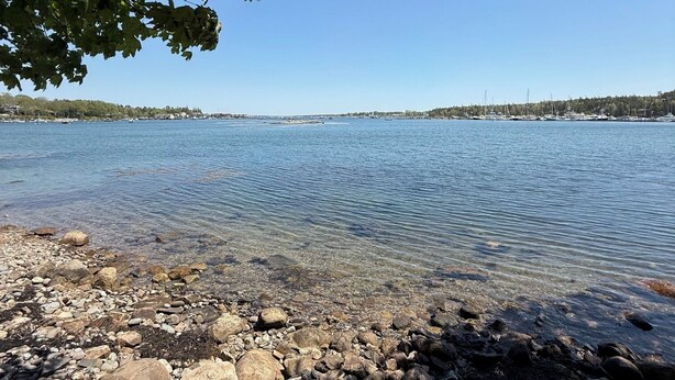 On aperçoit clairement un lac, avec une rive rocheuse et des bateaux au loin.