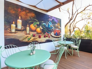 A dining area with a mural, green metal chairs, and round tables. - Brada Collection Stays (Guadalajara)