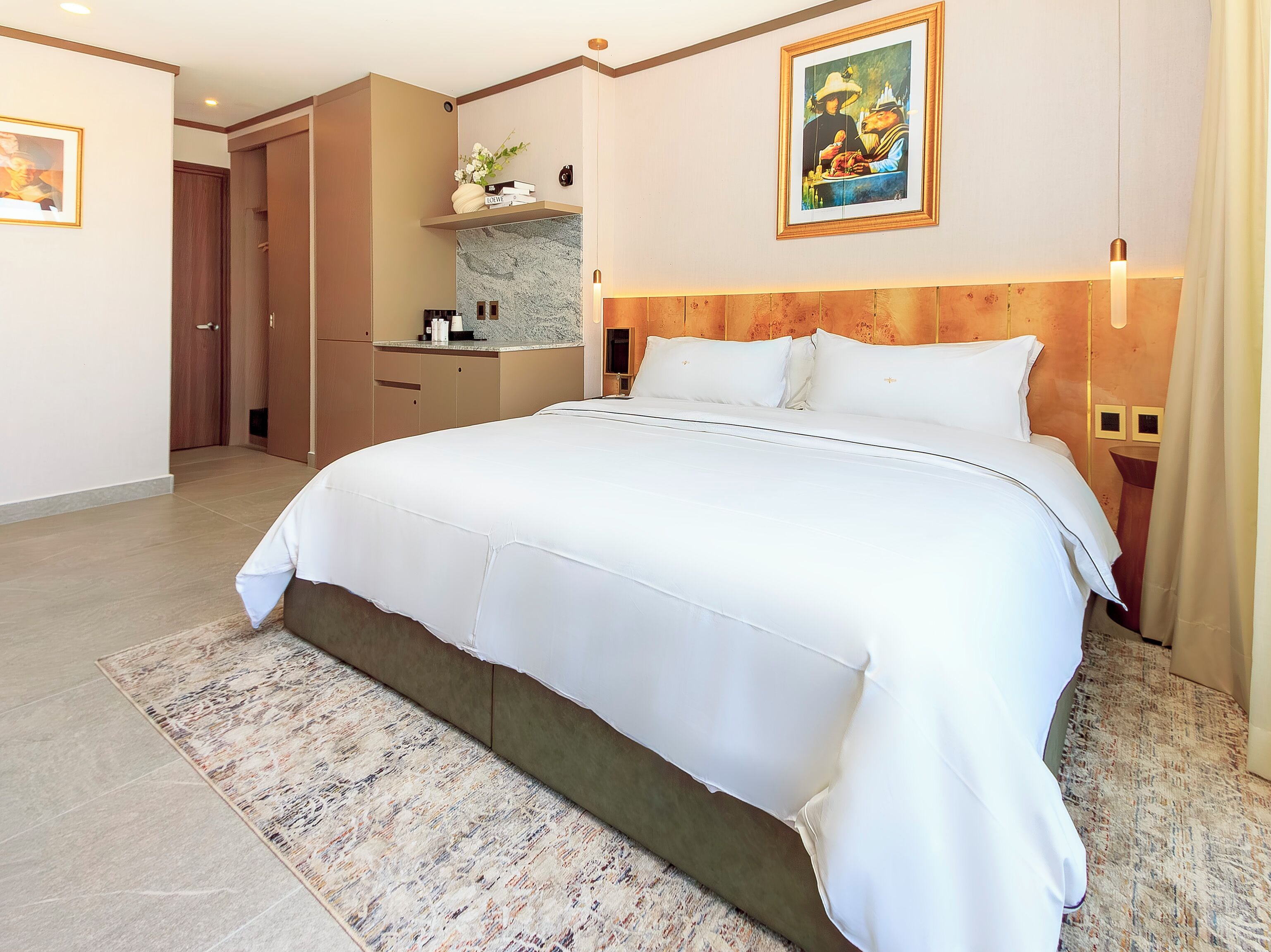 A hotel room with a large bed, a wooden headboard, a small bathroom, and a dining area.