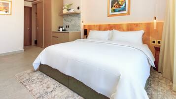 A hotel room with a large bed, a wooden headboard, a small bathroom, and a dining area.