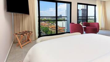 Habitación de hotel con una cama grande, dos sillas rojas, un televisor y vistas a la ciudad.