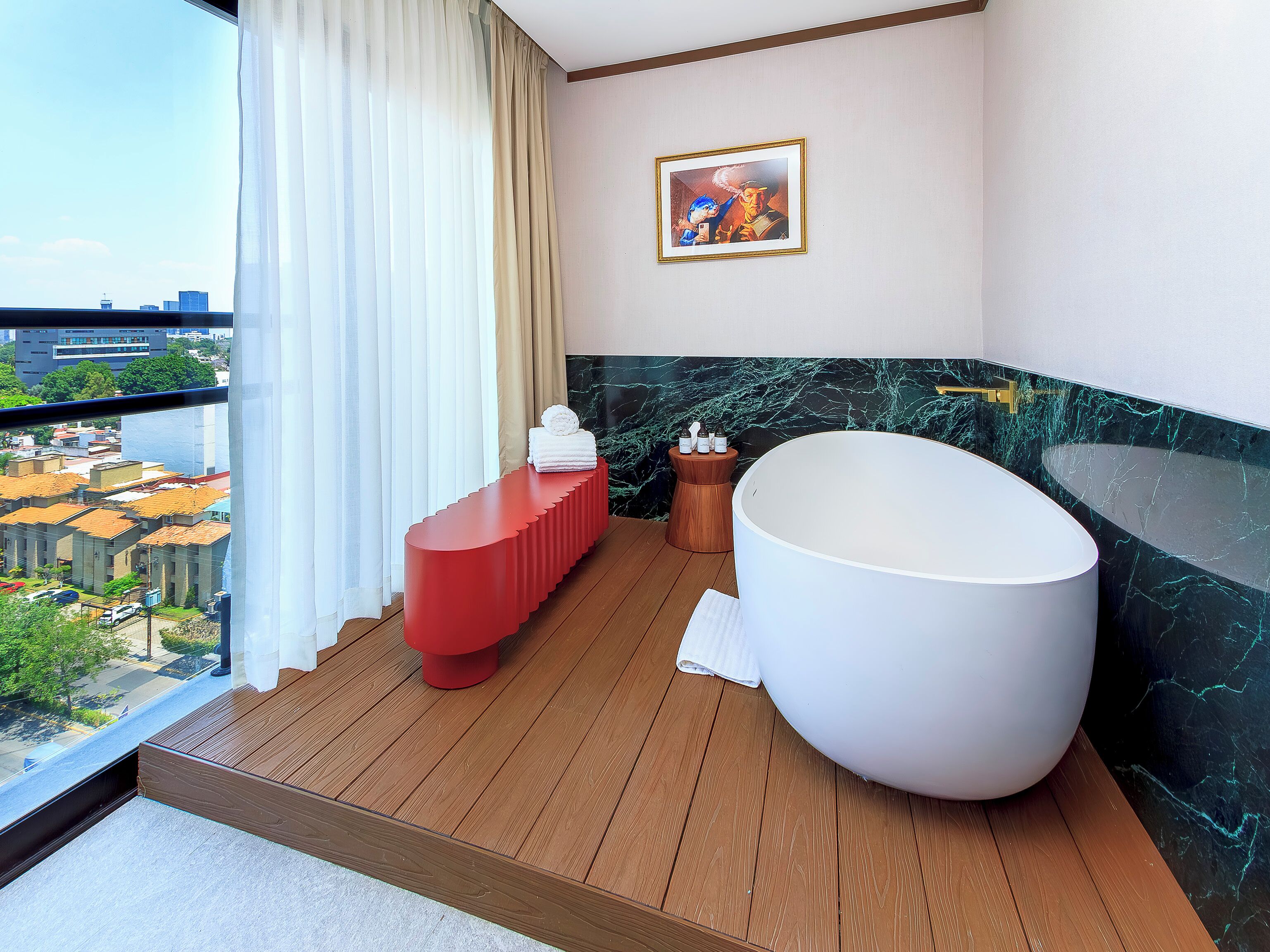 A modern bathroom with a large bathtub, a red bench, and a marble wall.
