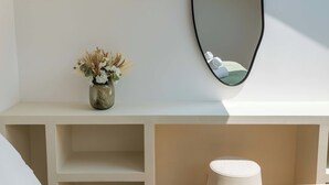 A minimalist room with a white console table, a vase with dried flowers, a round mirror, and a white cylindrical object on the floor.