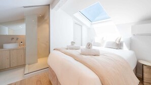 A modern bedroom with a skylight, a large bed, a walk-in shower, and a minimalist bathroom.